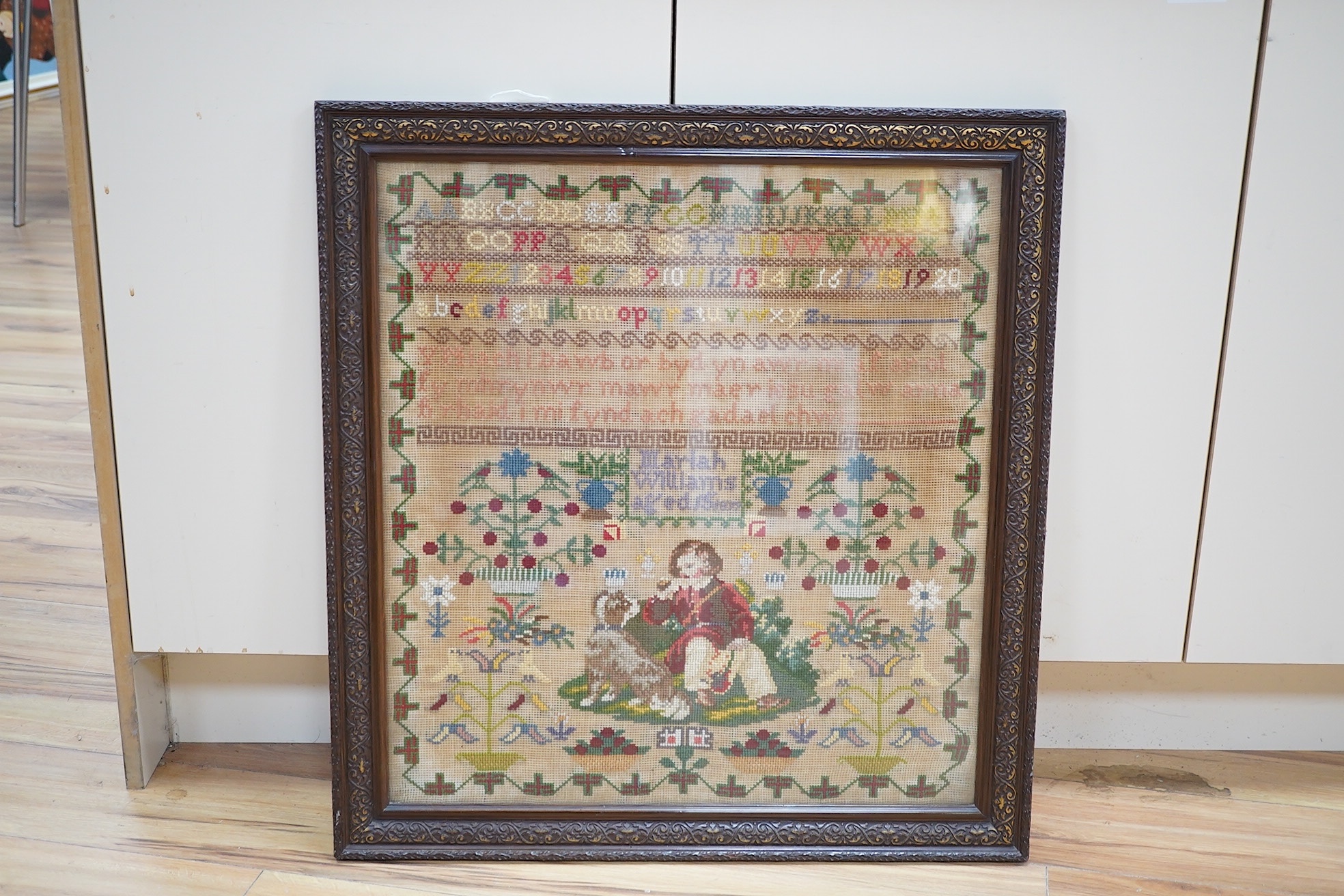 A 19th century cross stitch sampler by Mariah Williams age 15 dated 1879, worked with an outer geometric border, with rows of various alphabet letters and numerals., the lower half with large spot motifs of flowers, tree